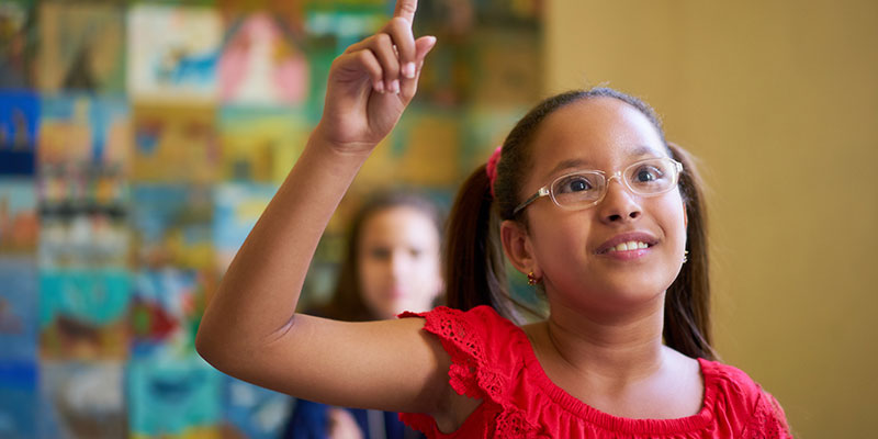 A Hispanic girl raises her hand in class